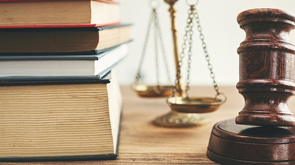 Zoom in of books stacked up, next to scales and a gavel on a wood table top